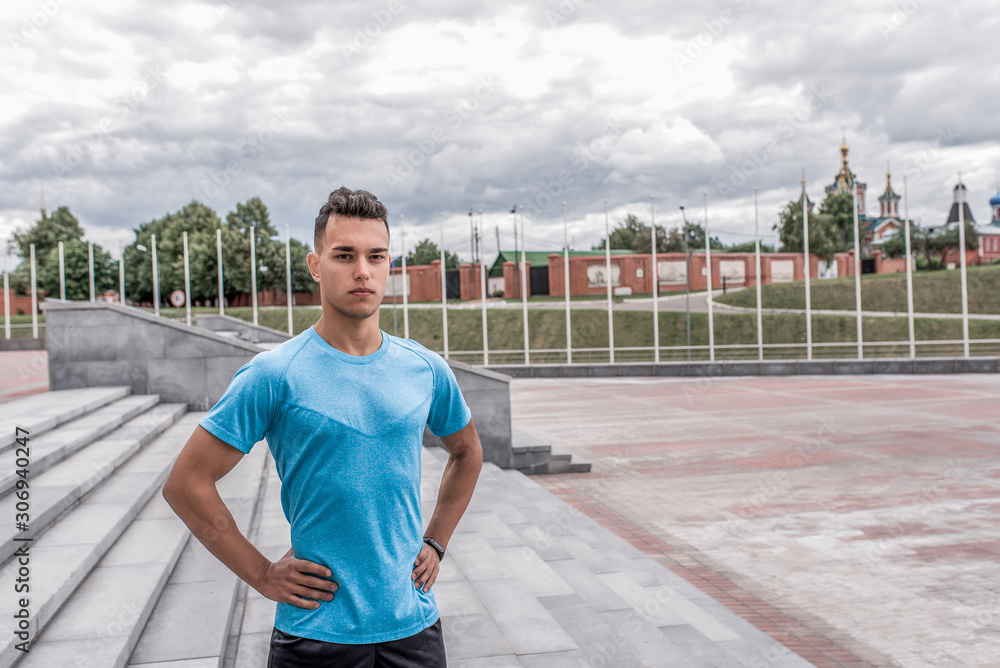 male athlete posing and looking confidently, coach controls in summer in city. Fitness motivation youth lifestyle. Free space for copy text. Background stairs, clouds.