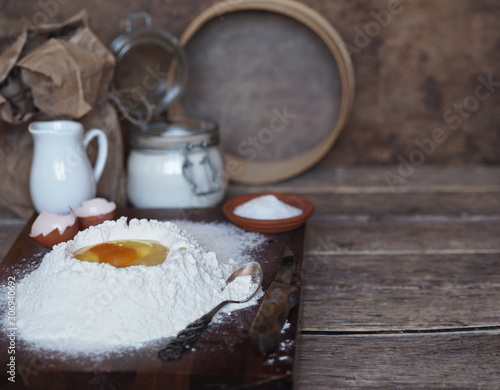 egg in flour to cook dough with ingredients on a wooden brown background