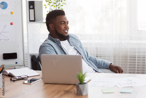 Successful black businessman sitting at workplace with glad face expression