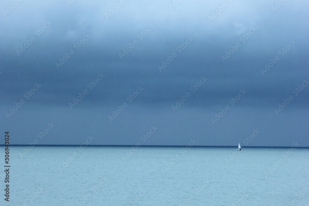 Small white yacht, turquoise blue sea and dark blue sky with clouds, a rainy day