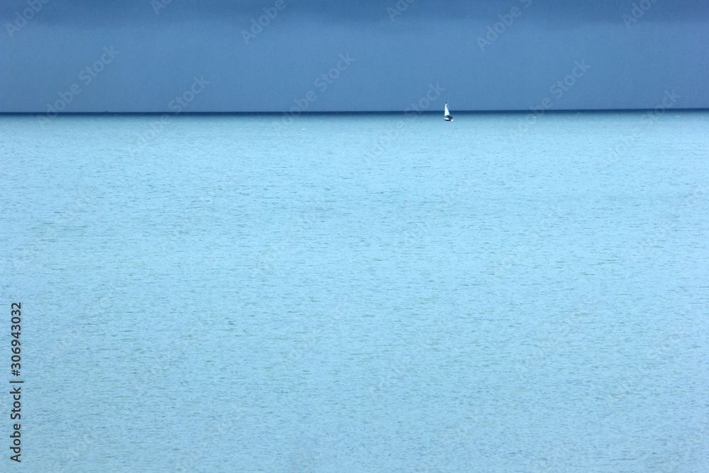 Obraz premium Small white yacht, turquoise blue sea and dark blue sky with clouds, a rainy day