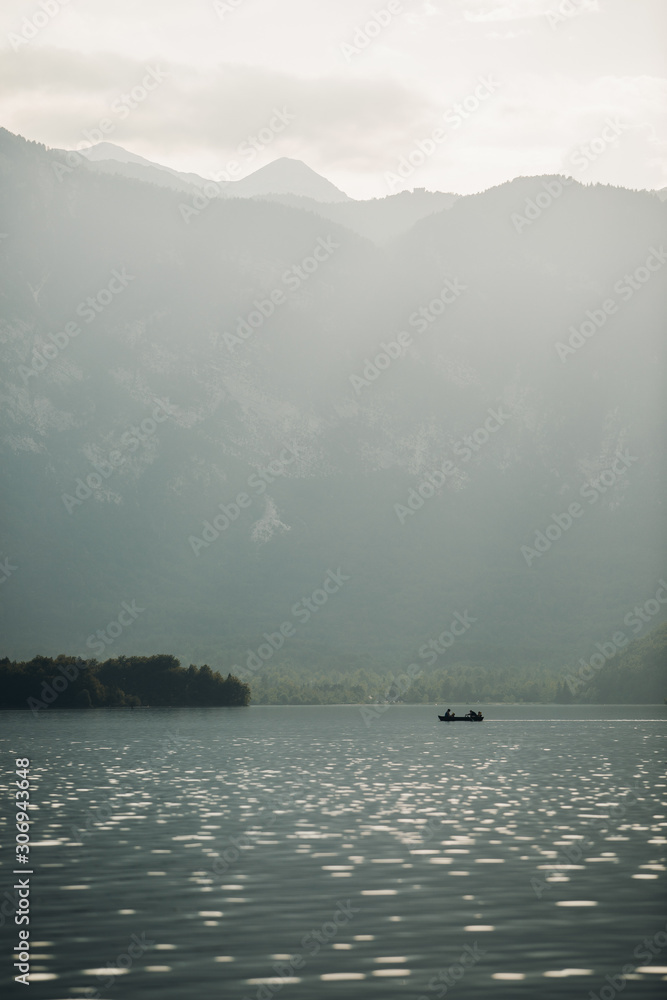 Silhouette of fishermen in a small boat on a lake at first Light. Early morning sunrise, boating on the lake in the sunlight. Peaceful landscape of a boat on the calm water. 