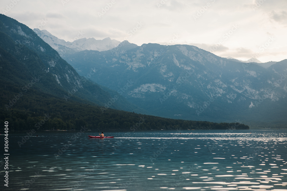 Kayaking at sunset in the mountains. Lake Kayak Touring. Man in red canoe on Lake Bohinj, Slovenia. Summer Recreations and Sport Photo Concept. 