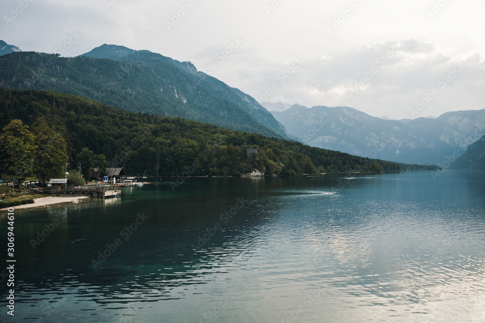 Mountain lake with clean water. Small village on the coast, a tourist destination. Lake in the foreground, misty mountains in the background. Lake Bohinj, Slovenia, Triglav National Park