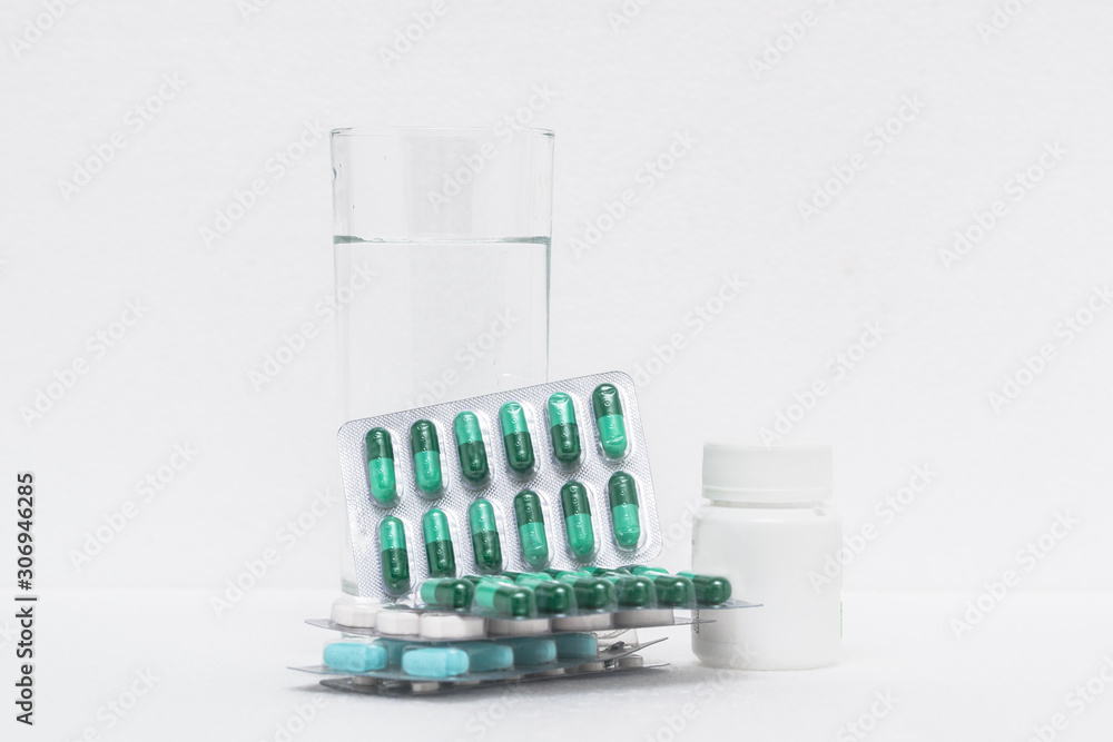 Medicines such as capsules, tablets and a glass of water are placed on a white background Medicines such as capsules, tablets and a glass of water are placed on a white background