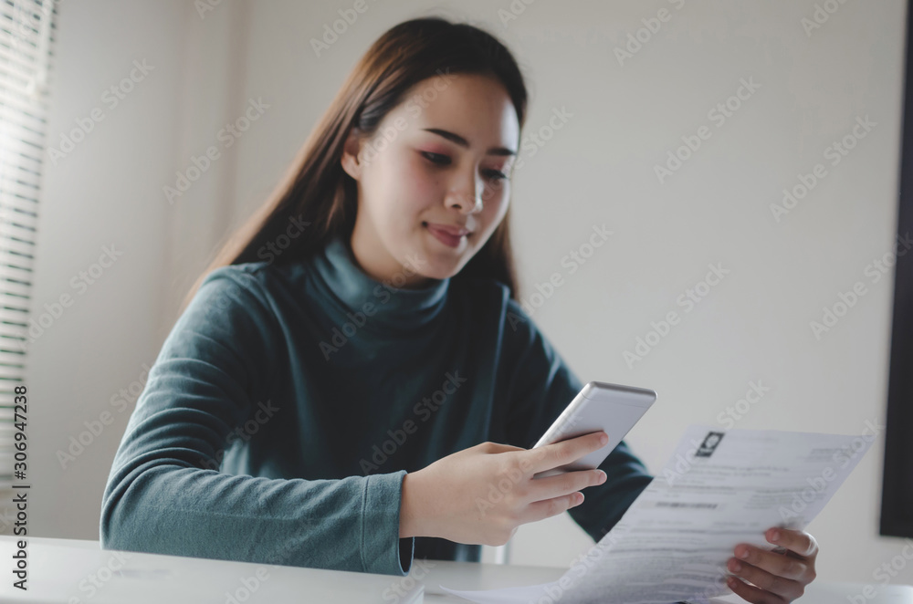 selective focus hand of asian young woman using mobile phone scan and payment online with family budget cost bills on desk in home, money cost saving, investment, business finance and expenses concept selective focus hand of asian young woman using mobile phone scan and payment online with family budget cost bills on desk in home, money cost saving, investment, business finance and expenses concept
