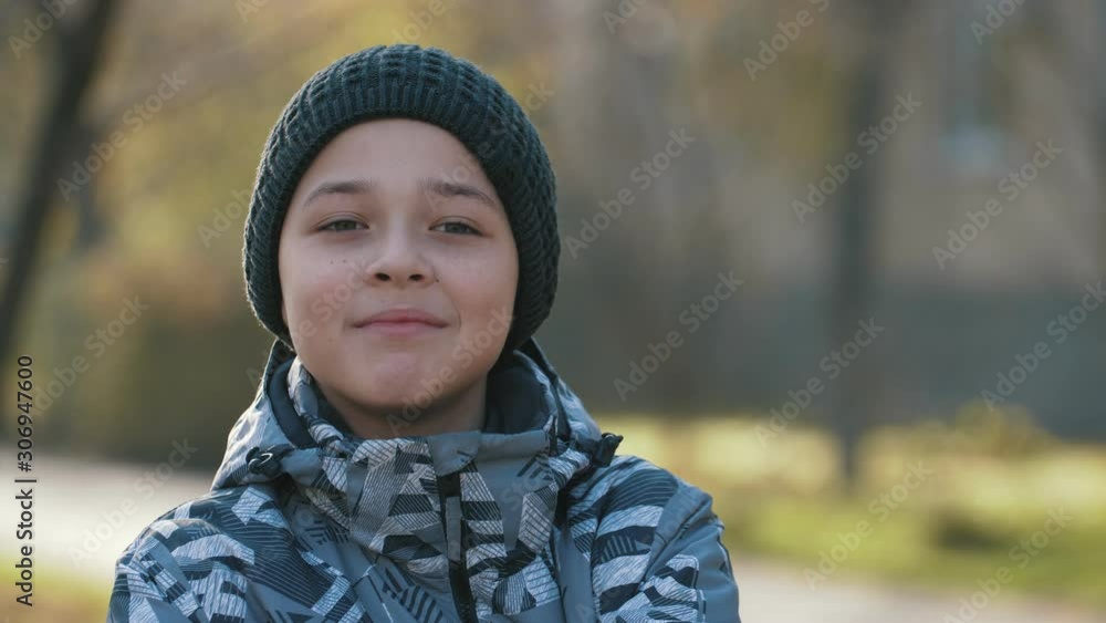 Happy brunet boy in a hat standing and smiling outdoors in sunny park in autumn Happy brunet boy in a hat standing and smiling outdoors in sunny park in autumn