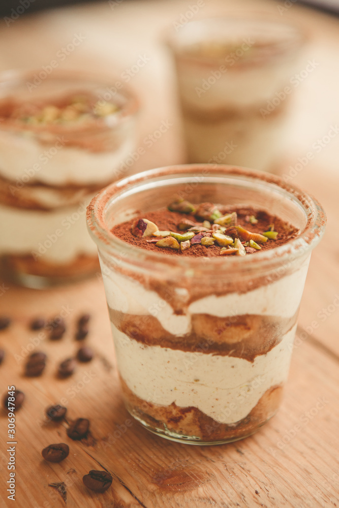 Tiramisu with pistachios and coffee in jars on a wooden countertop Tiramisu with pistachios and coffee in jars on a wooden countertop