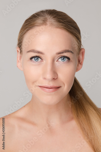 Studio portrait of attractive blonde caucasian woman with blue eyes and bare shoulders over white background. She is looking at camera with eyes wide open. Pure, smooth and flawless skin concept.