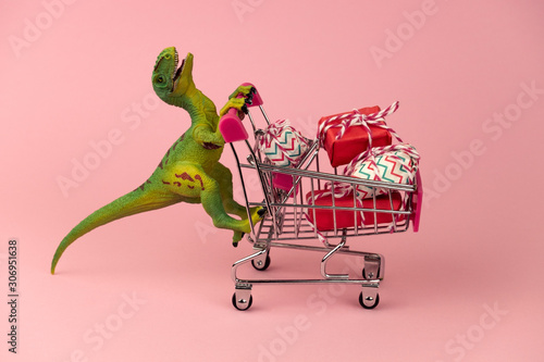 Photography funny green dinosaur toy with shopping cart full of present boxes on a soft pink
