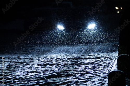 snowflakes during snowfall lit with light from car headlights at night on a road