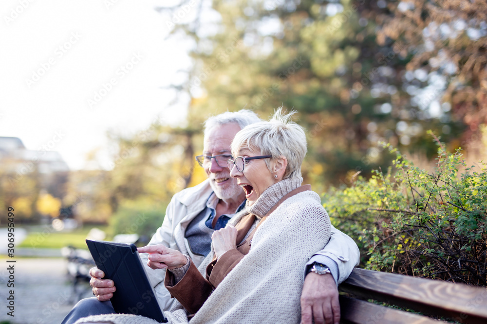 Senior couple sitting in the park on bench and shopping on line with tablet and credit card Senior couple sitting in the park on bench and shopping on line with tablet and credit card