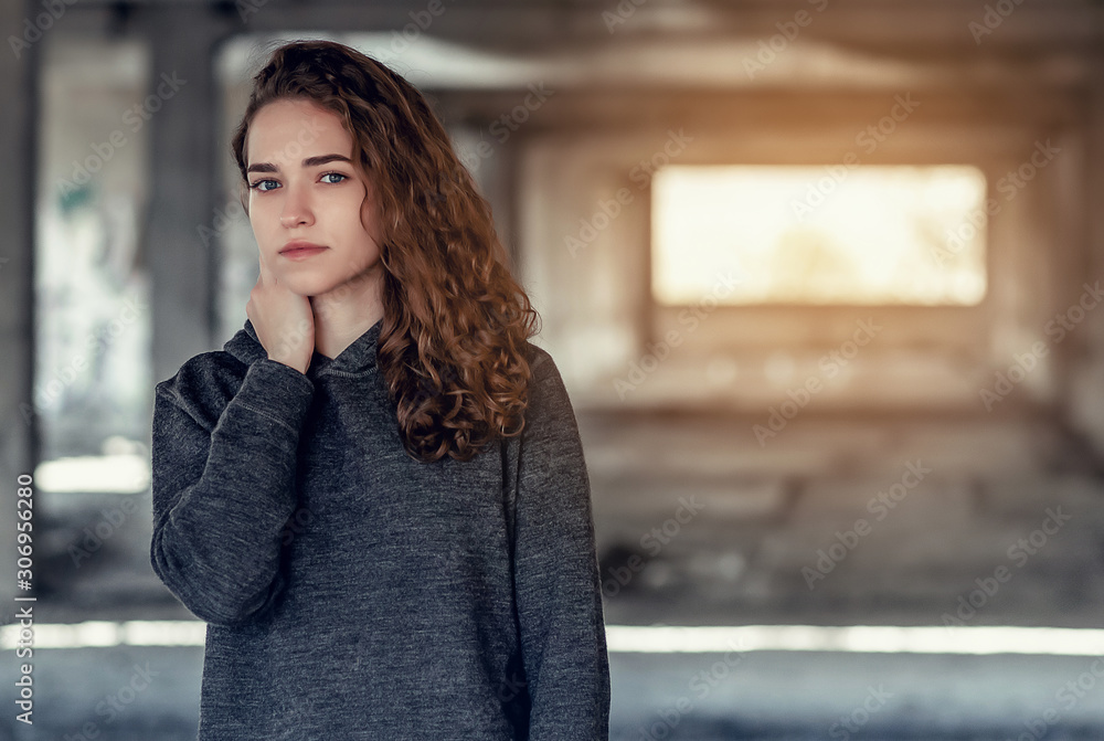 Fototapeta premium Curly hair. Beautiful girl on background of an abandoned concrete building. Light from behind at the industrial area.