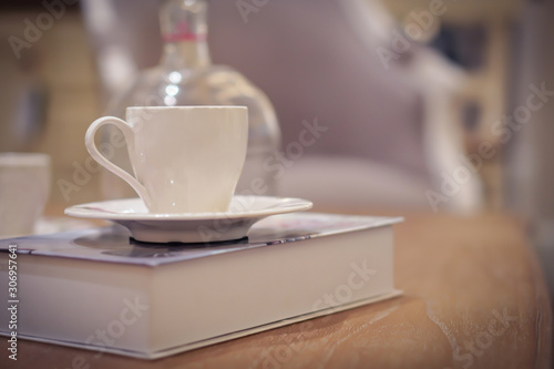 Focus selection: A white coffee cup placed on a book at a table and a glass bottle near it. In a light, comfortable atmosphere