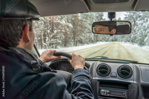 Man driving car on snowy country road through snow covered forest in winter cloudy day. Weekend roadtrip in bad weather, travel concept. Inside view, selective focus © Tatyana_Andreyeva