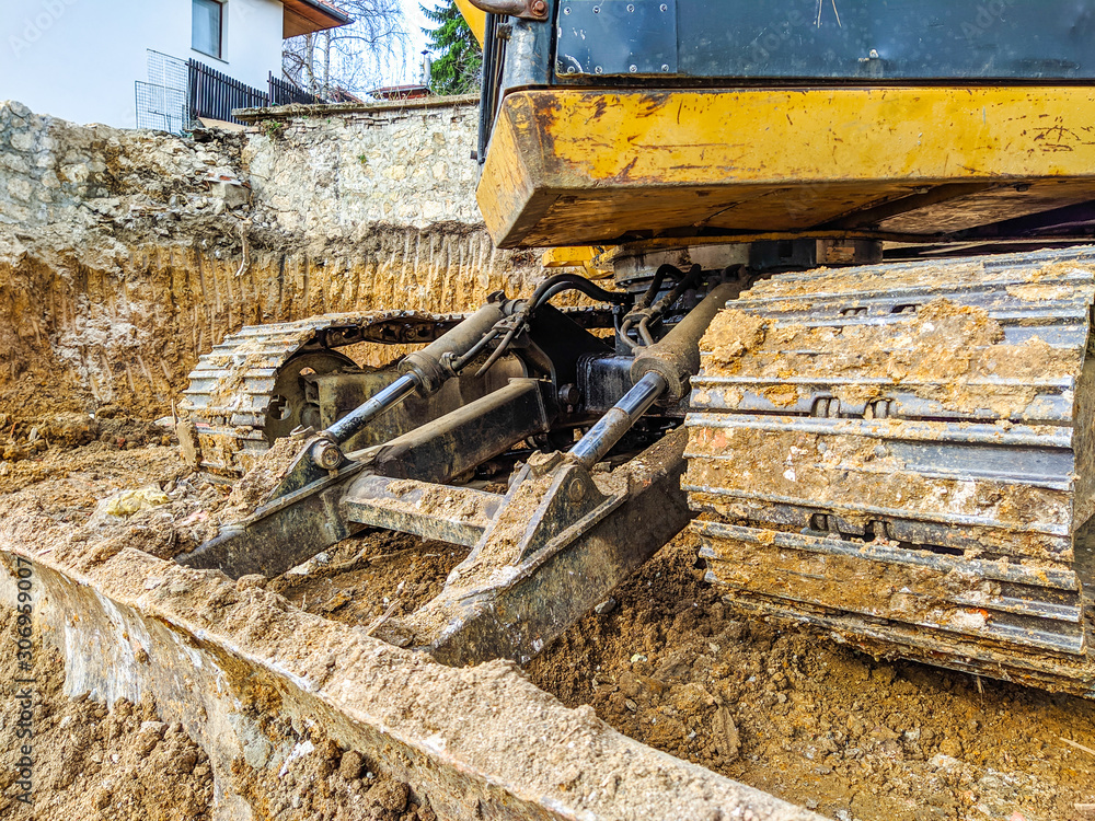 Fototapeta premium Yellow bulldozer excavator shoveling and digging the ground while working on the difficult excavation, new modern industrial machinery for heavy work