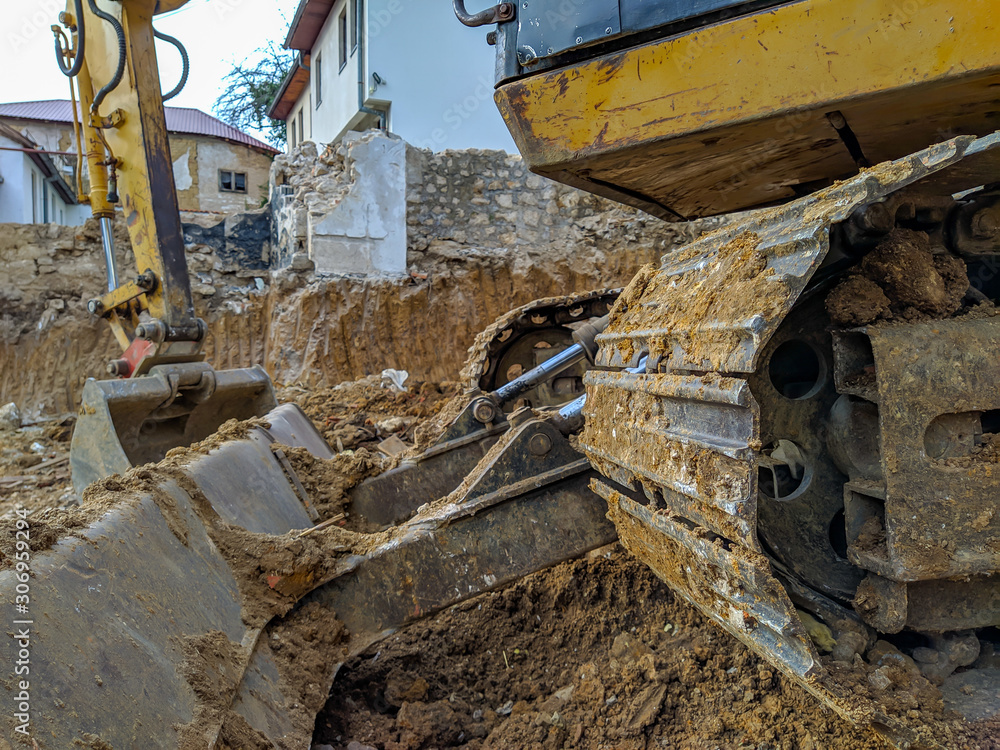 Fototapeta premium Closeup of yellow digger, bulldozer or excavator working on the site excavation, digging up the ground for new modern construction to take place
