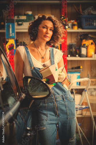 adorable woman car mechanic in blue overalls with a book-instruction