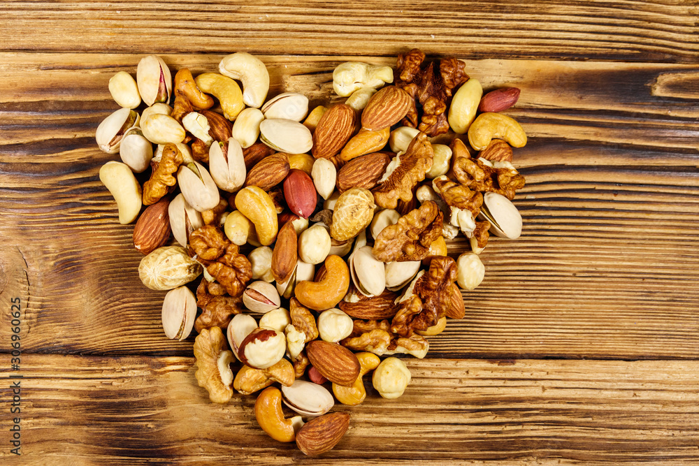 Pile of mixed nuts in shape of heart on wooden table. Top view. Walnuts, pistachio, almond, peanut, cashew, hazelnut on wood background. Healthy eating concept