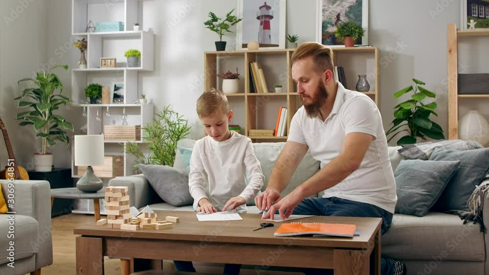 Father and son make paper planes in the living room
