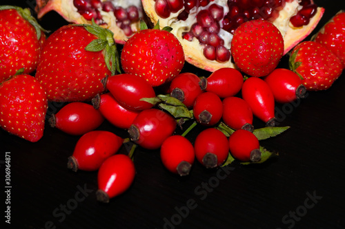 fresh red fruit on black background. Strawberries, pomegranate, briers on the table with free copy space