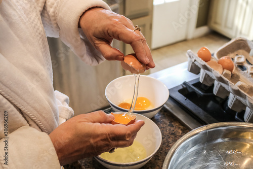 Hands of mature woman in bathrobe separating eggs on island in kitchen - Selective focus