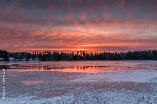 Fototapeta Naklejka Na Ścianę i Meble -  A fiery sunrise reflects off of the ice of a frozen lake in Northwest Ontario, Canada.