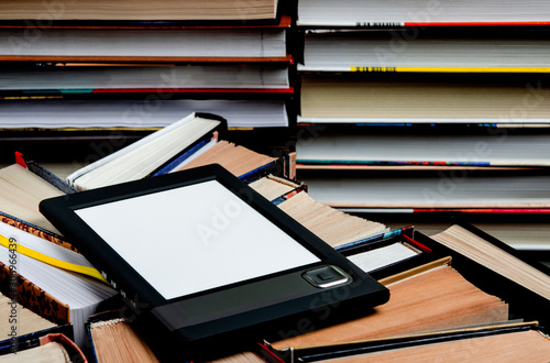 The e-book with a white screen lies on the open multi-colored books that lie on a dark background, close-up