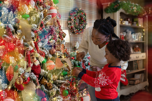 Little afro girl decorating Christmas tree with mother at home