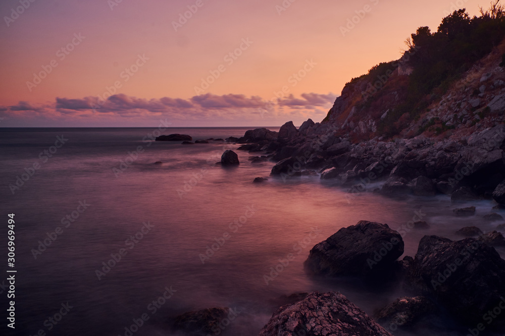Long exposure photography of the sea waves splashing near to the clif when the sun is going down