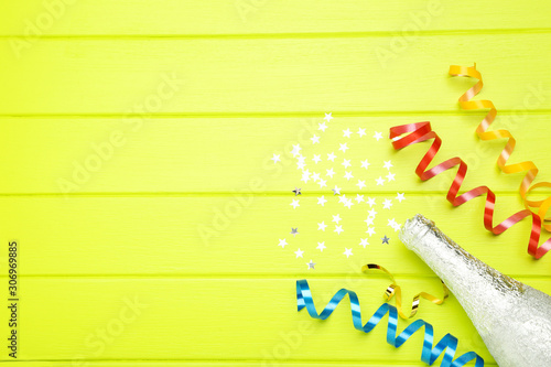 Colorful ribbons with stars and champagne bottle on green wooden background