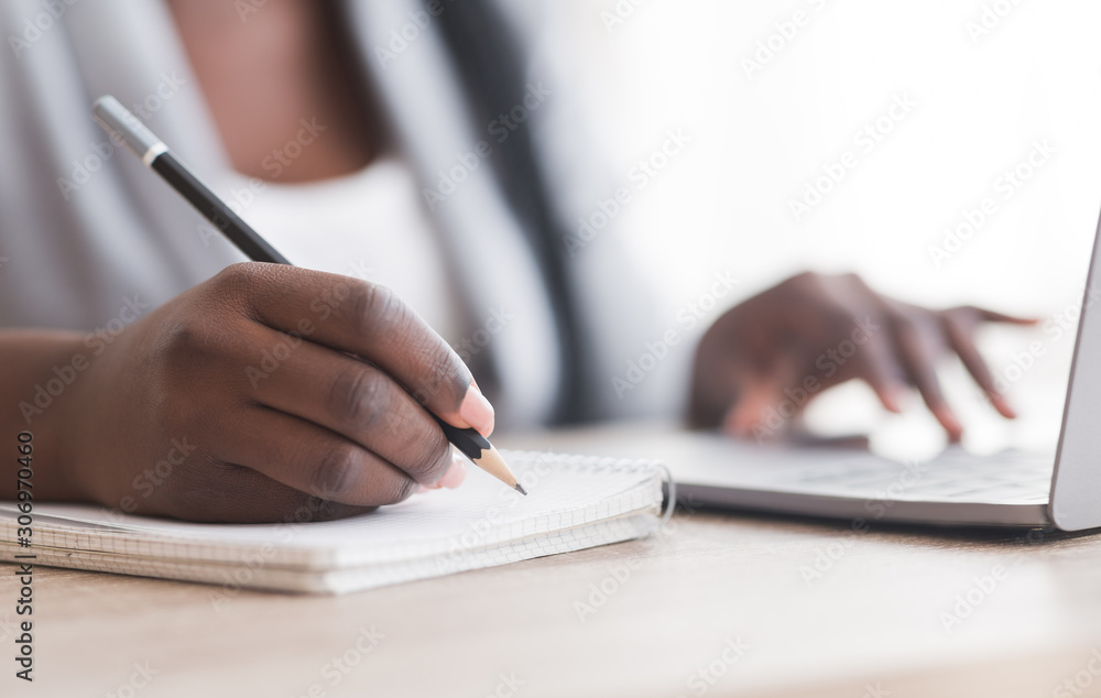 Unrecognizable female employee taking notes while working on laptop in office Unrecognizable female employee taking notes while working on laptop in office