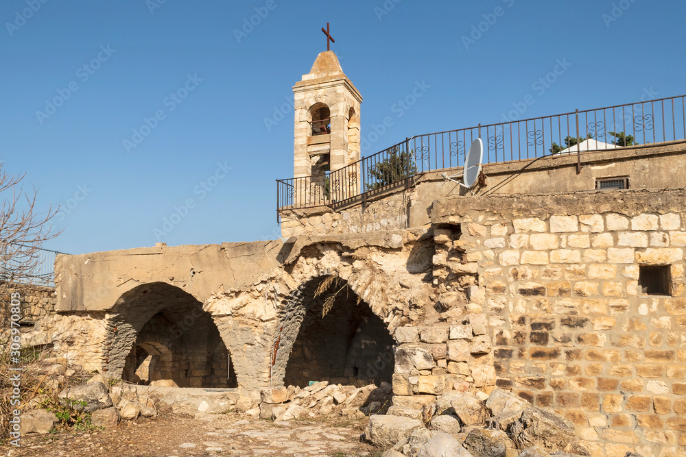 back of the ancient stone maronite church in baraam national park in israel showing two arches and the bell tower with a clear blue sky background