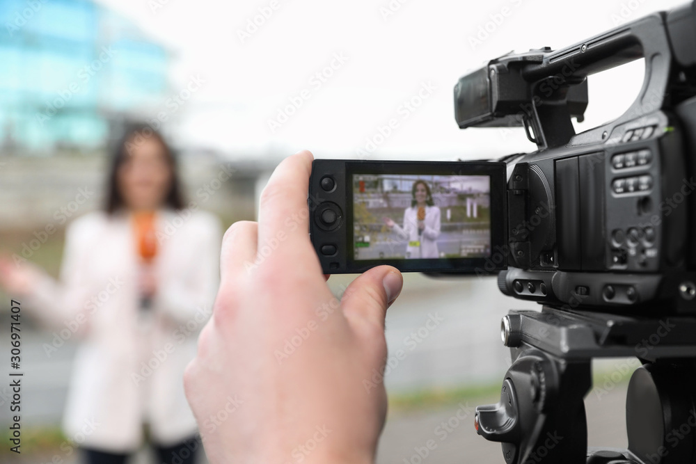 Young male journalist and video operator working on city street, focus on camera display