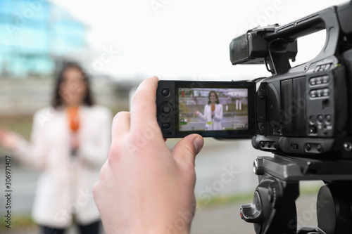 Young male journalist and video operator working on city street, focus on camera display