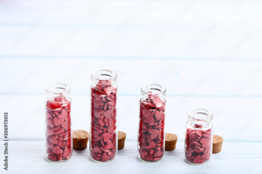 Red heart shaped sprinkles in glass bottles on wooden table Red heart shaped sprinkles in glass bottles on wooden table