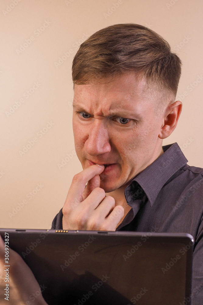 A series of photographs of a young man looking at a cyrus tablet with different emotions from happy with success to surprise and anger when using a phone on a gray background. A series of photographs of a young man looking at a cyrus tablet with different emotions from happy with success to surprise and anger when using a phone on a gray background.