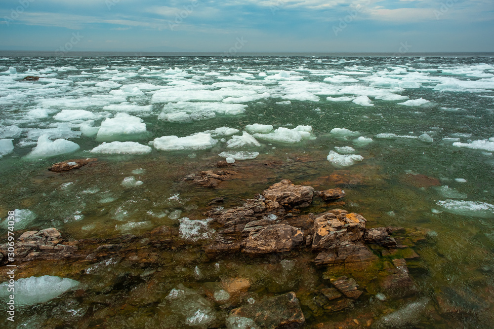 The view from the rocks in the foreground of a snow-white fragments of ice floes. Northern nature. Melting ice on lake Baikal