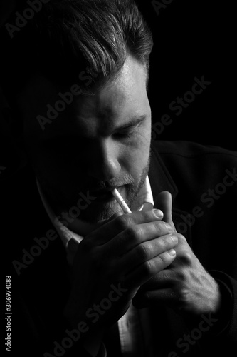 hipster young man smokes a cigarette. the guy is focused and serious on a dark background. black and white photo