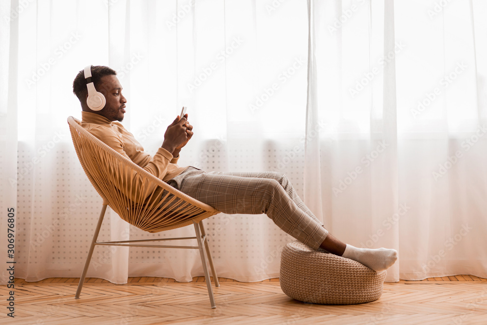 Relaxed Black Man In Headset Using Phone Listening Audiobook Indoor - obrazy, fototapety, plakaty 
