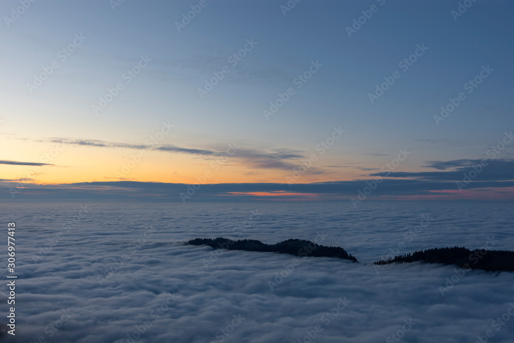 Some hills sticking out of a sea of clouds after sunset. Atmospheric and colorful scene. Bavaria, Germany. Copy space
