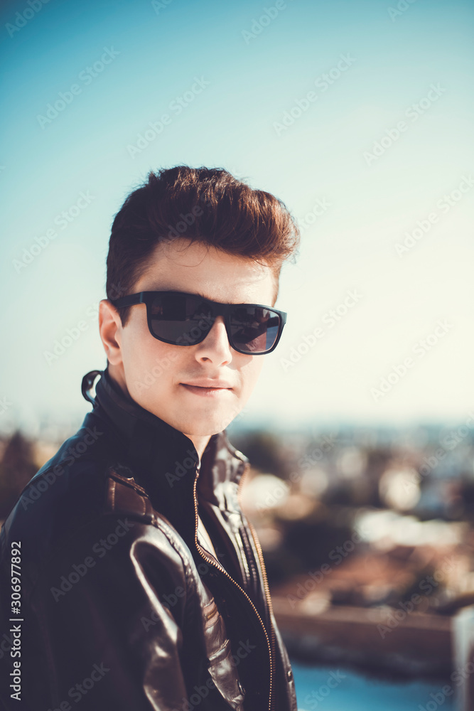Young attractive man posing in front of camera in a dark brown jacket on the roof of a residential building Young attractive man posing in front of camera in a dark brown jacket on the roof of a residential building