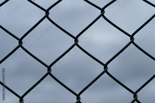 Details of a wire-mesh fence in front of the dark and cloudy sky - security concept