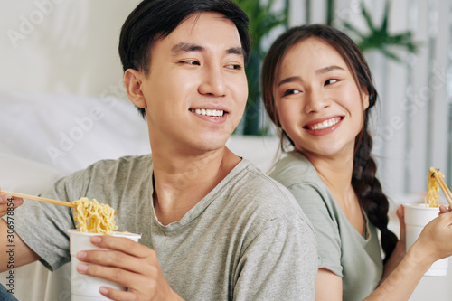 Happy young Asian couple enjoying tasty instant ramen soup for dinner at home