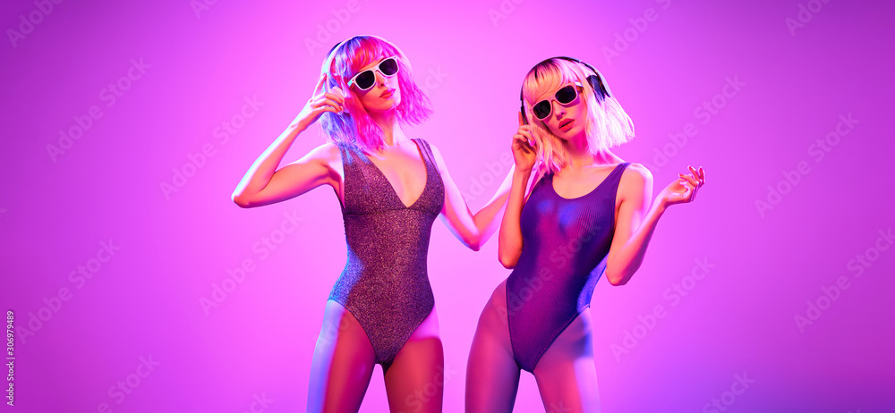 Two sexy fashionable DJ girl in party outfit dance. Colorful neon uv light. Party night club vibes, gel filter. Excited woman with Dyed Hair, makeup. High Fashion. Creative Bright pink neon color. Two sexy fashionable DJ girl in party outfit dance. Colorful neon uv light. Party night club vibes, gel filter. Excited woman with Dyed Hair, makeup. High Fashion. Creative Bright pink neon color.