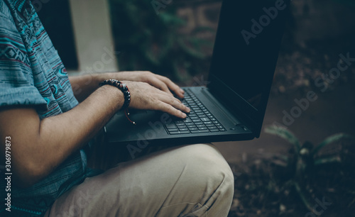 Young Hispanic man on the sidewalk of his house checking the black computer