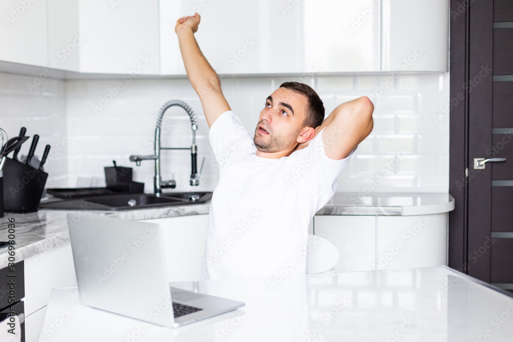 Yawning sleepy man yawn working on his laptop in kitchen in the morning. Yawning sleepy man yawn working on his laptop in kitchen in the morning.