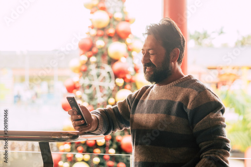Caucasian man using mobile phone in winter christmas period with tree in background at commercial mall center for shopping and buy gifts or presents for friends or parents photo