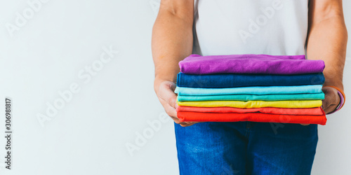 close up stack of folded multicolored t-shirt in hands over white background, copy space