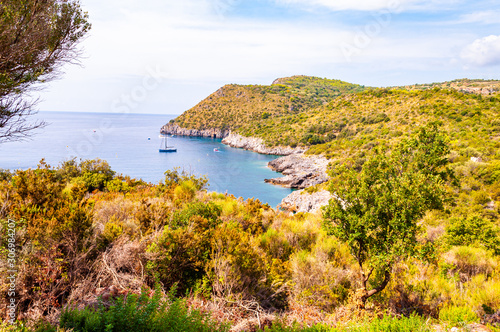 Scenic landscape view from the overgrown rocky mountains of Cilento and Vallo di Diano National Park in Campania, Italy on hidden Cala Bianca beach surrounded by rocks in Tyrrhenian sea
